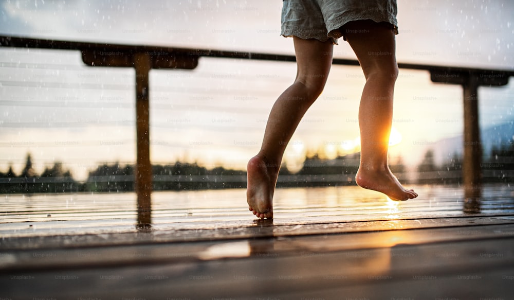 An unrecognizable small daughter playing in rain on patio of wooden cabin, holiday in nature concept.