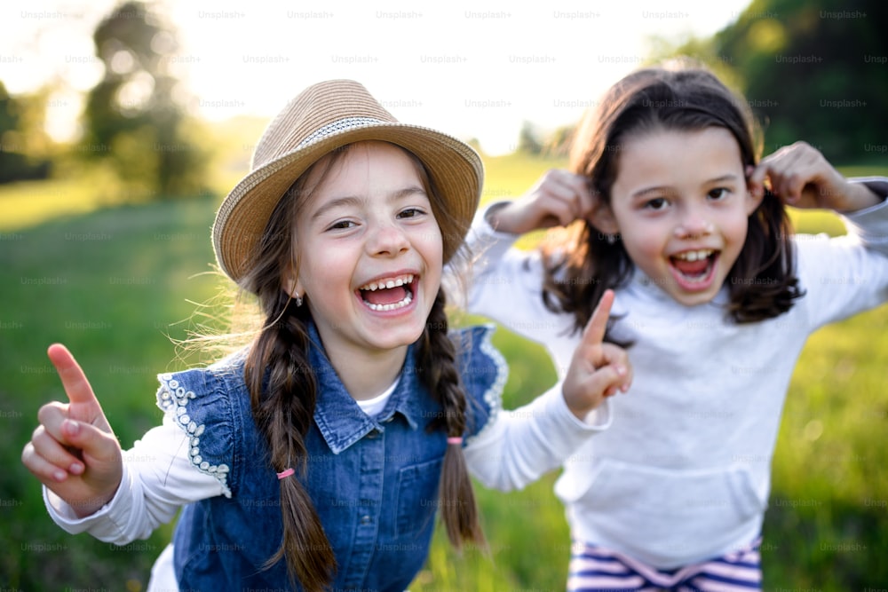 Front view portrait of two small girls standing outdoors in spring nature, laughing.
