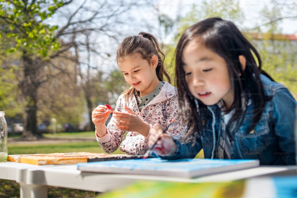 Portrait of small children painting pictures outdoors in city park, learning group education concept.