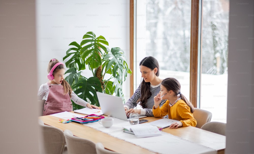Mother with school girls indoors at home, distance learning and home office coccept.