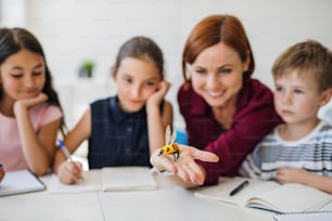Eine Gruppe kleiner Schulkinder mit Lehrer, die im Unterricht am Schreibtisch im Kreis sitzen und Naturwissenschaften lernen.