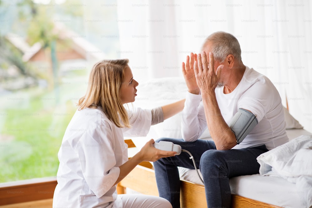 Visiteur de santé et un homme âgé lors d’une visite à domicile. Une infirmière vérifie la tension artérielle d’un homme.