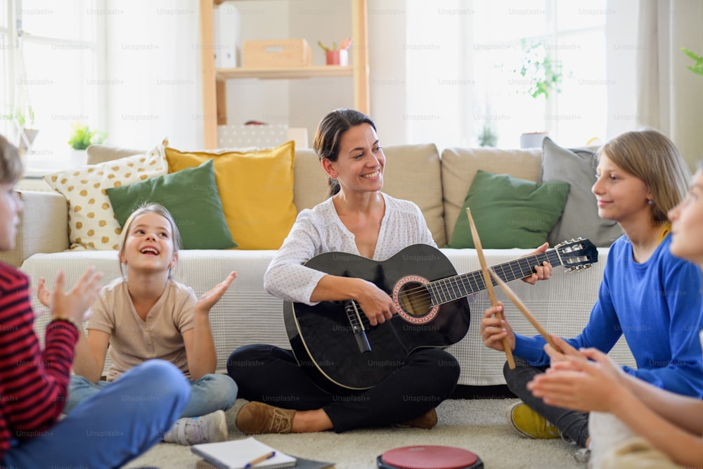 Group of cheerful homeschooling children with teacher having music lesson indoors, coronavirus concept.