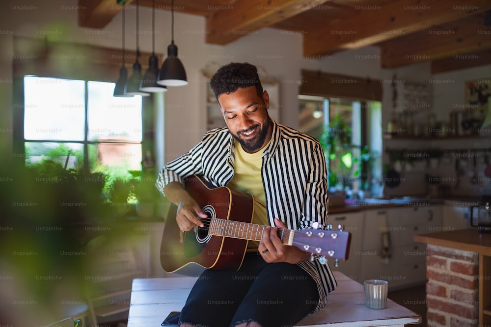 Portrait of happy young man with guitar indoors at home, relaxing.