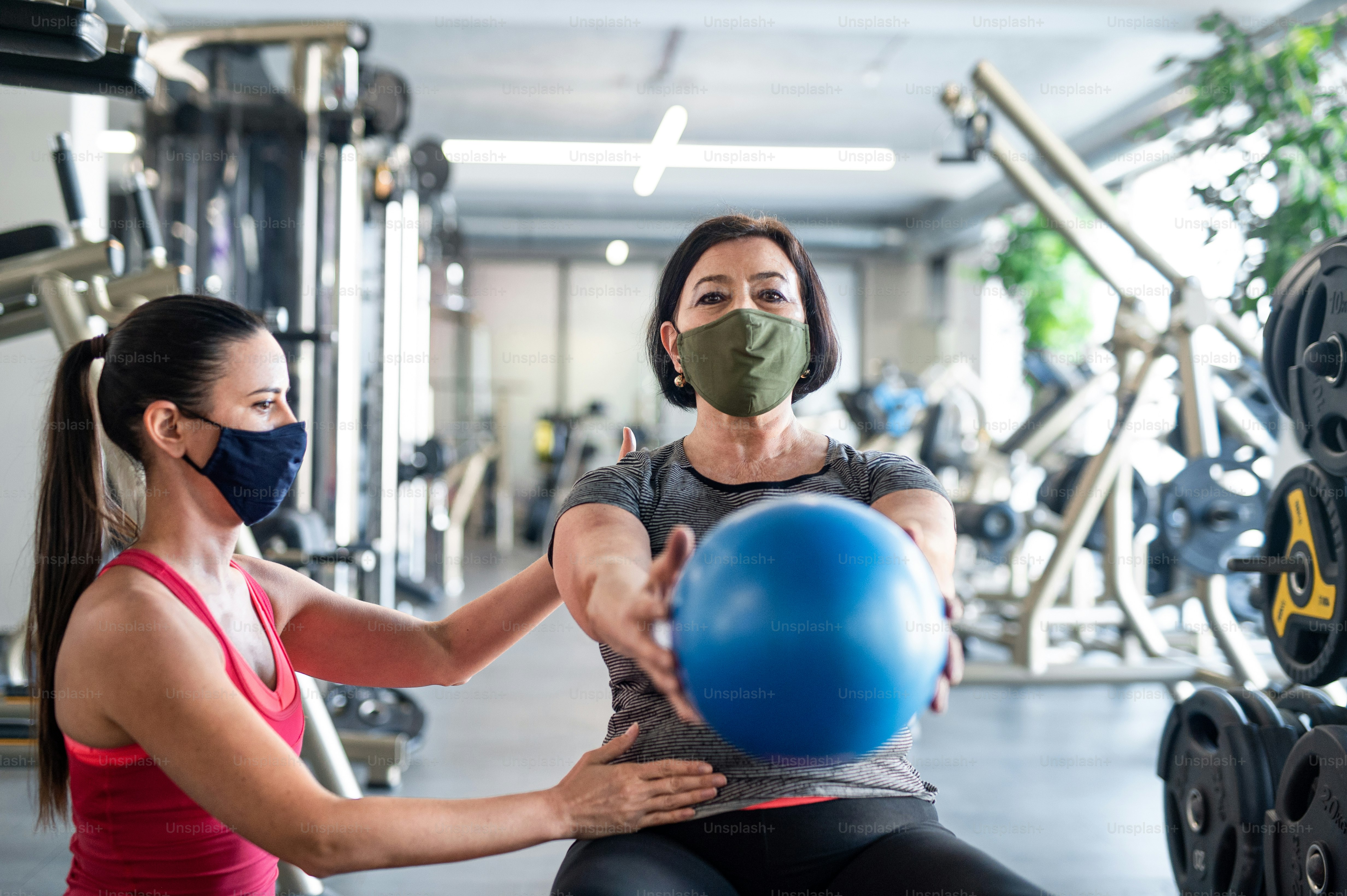 Active senior woman with personal trainer doing exercise in gym, coronavirus concept