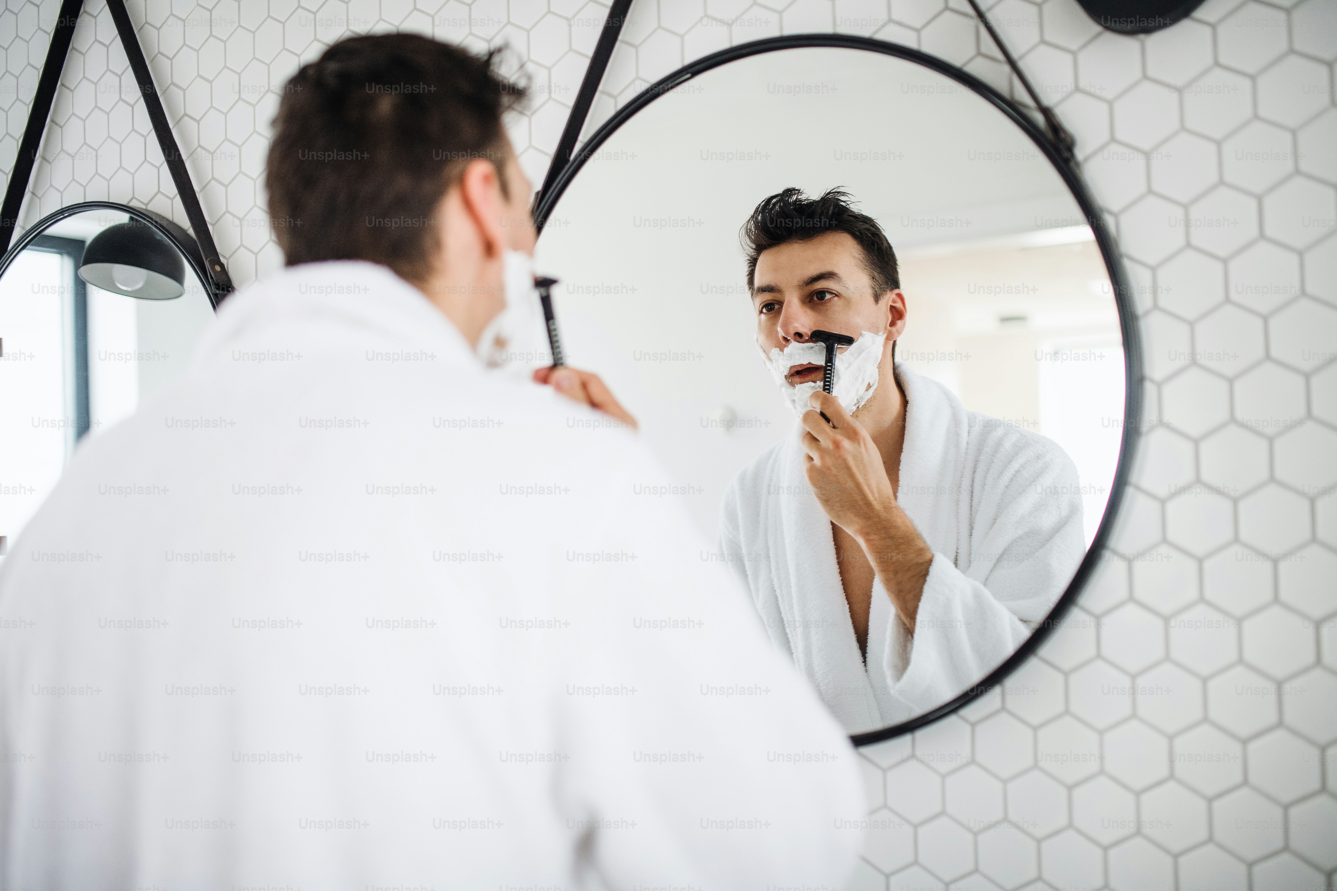 Ein junger Mann rasiert sich morgens im Badezimmer, eine tägliche Routine.