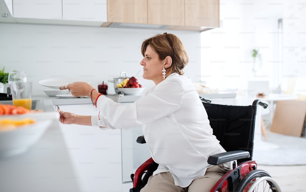 A portrait of disabled mature woman in wheelchair indoors at home, preparing breakfast.