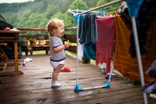 Two happy toddler children standing outdoors on a terrace in summer, playing with clothes drying hanger.