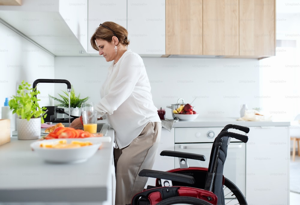 A portrait of disabled mature woman with wheelchair indoors at home, preparing breakfast.