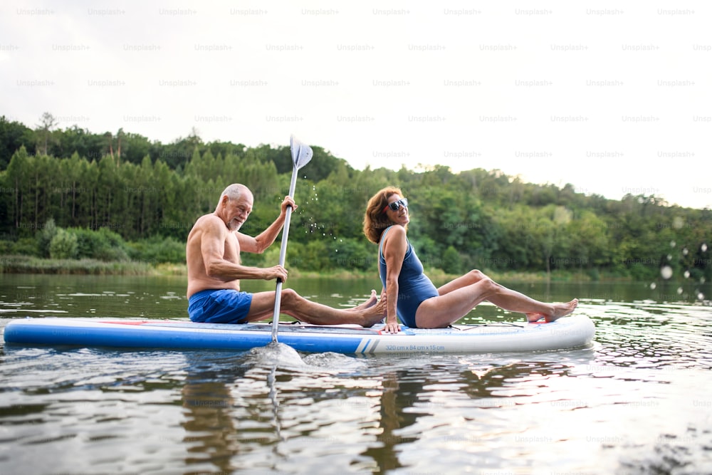 Active senior couple paddleboarding on lake in summer.