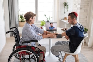 Pessoas com deficiência sentadas à mesa dentro de casa em casa, consulta on-line por vídeo com o médico.