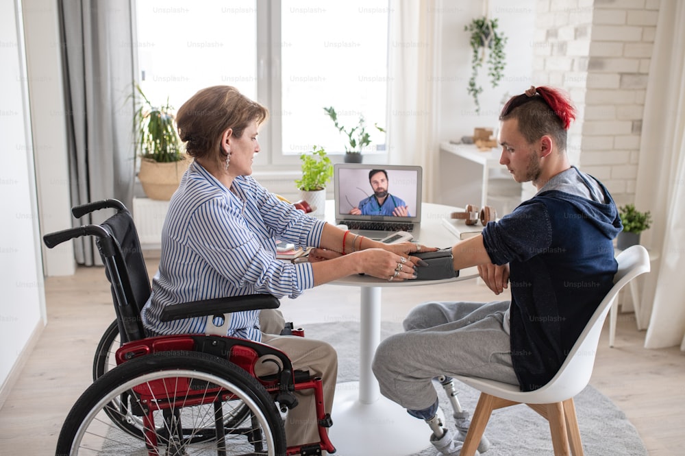 Personas discapacitadas sentadas en la mesa en el interior de casa, videoconsulta en línea con el médico.
