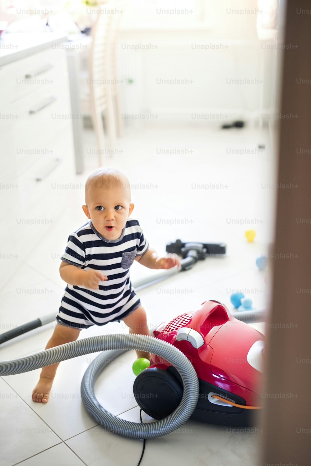 Cute baby boy with the hoover in the kitchen. Little boy playing with vacuum cleaner.