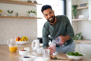 Portrait of young man preparing healthy breakfast indoors at home, looking at camera.