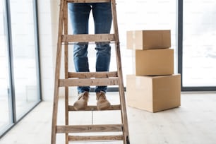 はしごの上に立ち、新しい家を整える段ボール箱を持つ男の中央部。新しい家のコンセプト。スペースをコピーします。