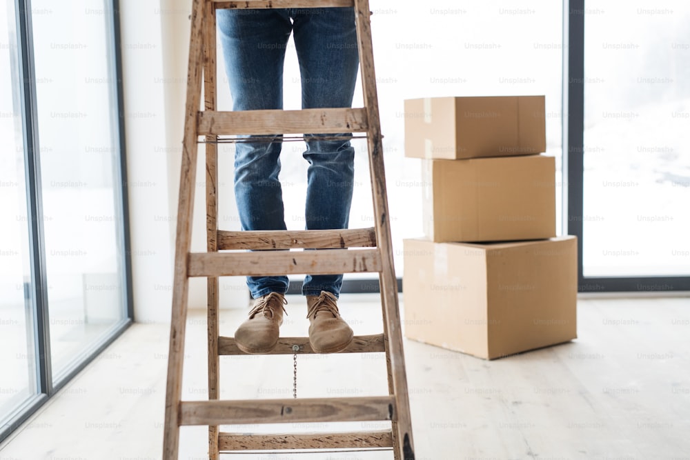 Un tronco di uomo con scatole di cartone in piedi su una scala, arredando una nuova casa. Un nuovo concetto di casa. Copia spazio.