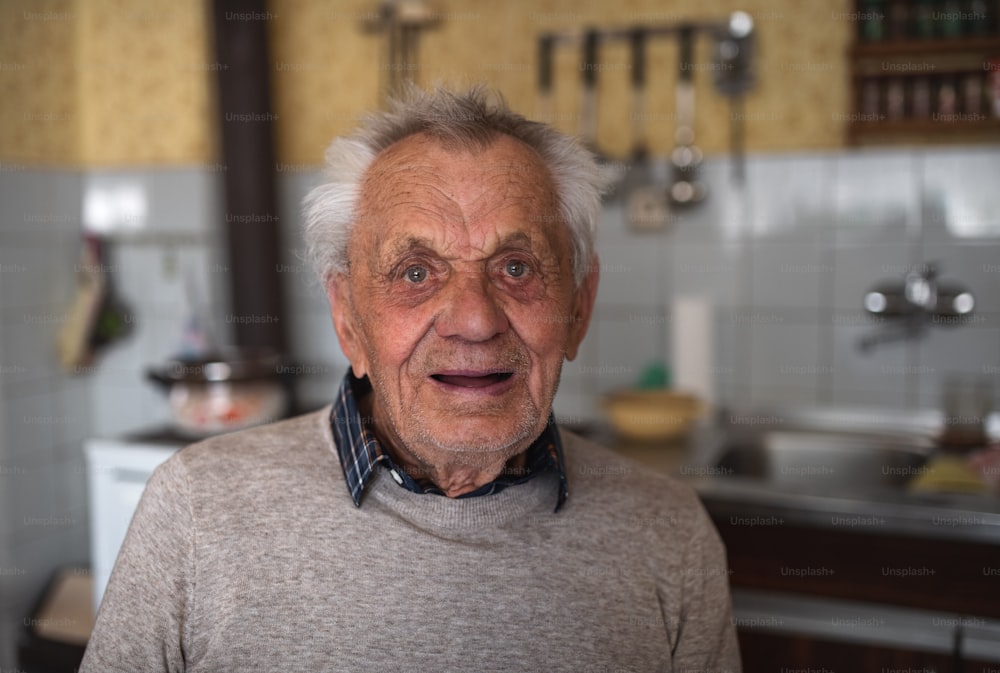 Un portrait d’un homme âgé debout à l’intérieur de la maison, riant.