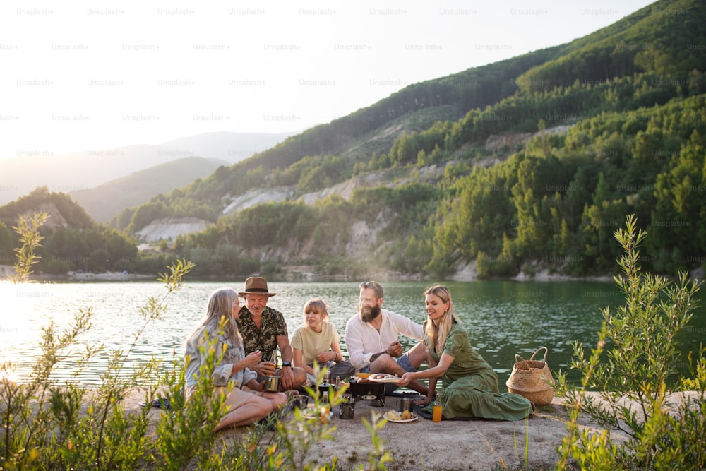 A happy multigeneration family on summer holiday trip, barbecue by lake.