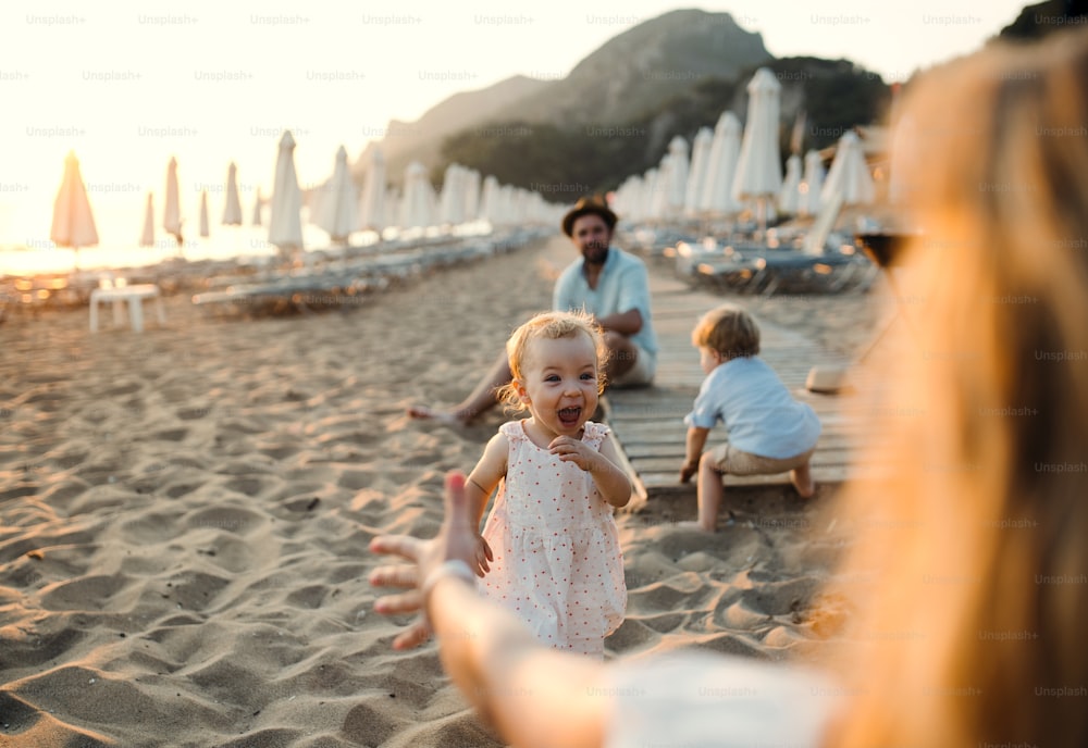 A young family with toddler children having fun on beach on summer holiday.