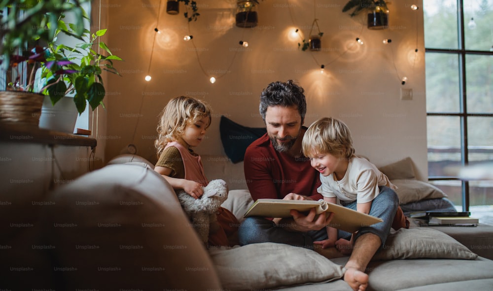 A mature father with two small children resting indoors at home, looking at photo album.