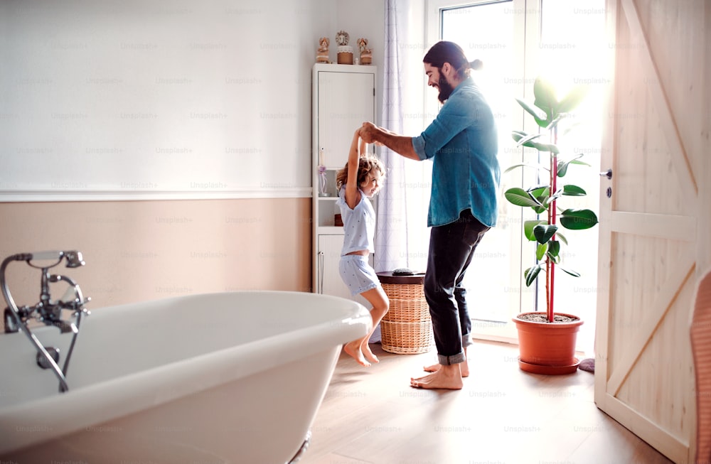 Uma menina pequena com pai jovem no banheiro em casa, se divertindo.