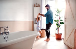 A small girl with young father in bathroom at home, having fun.