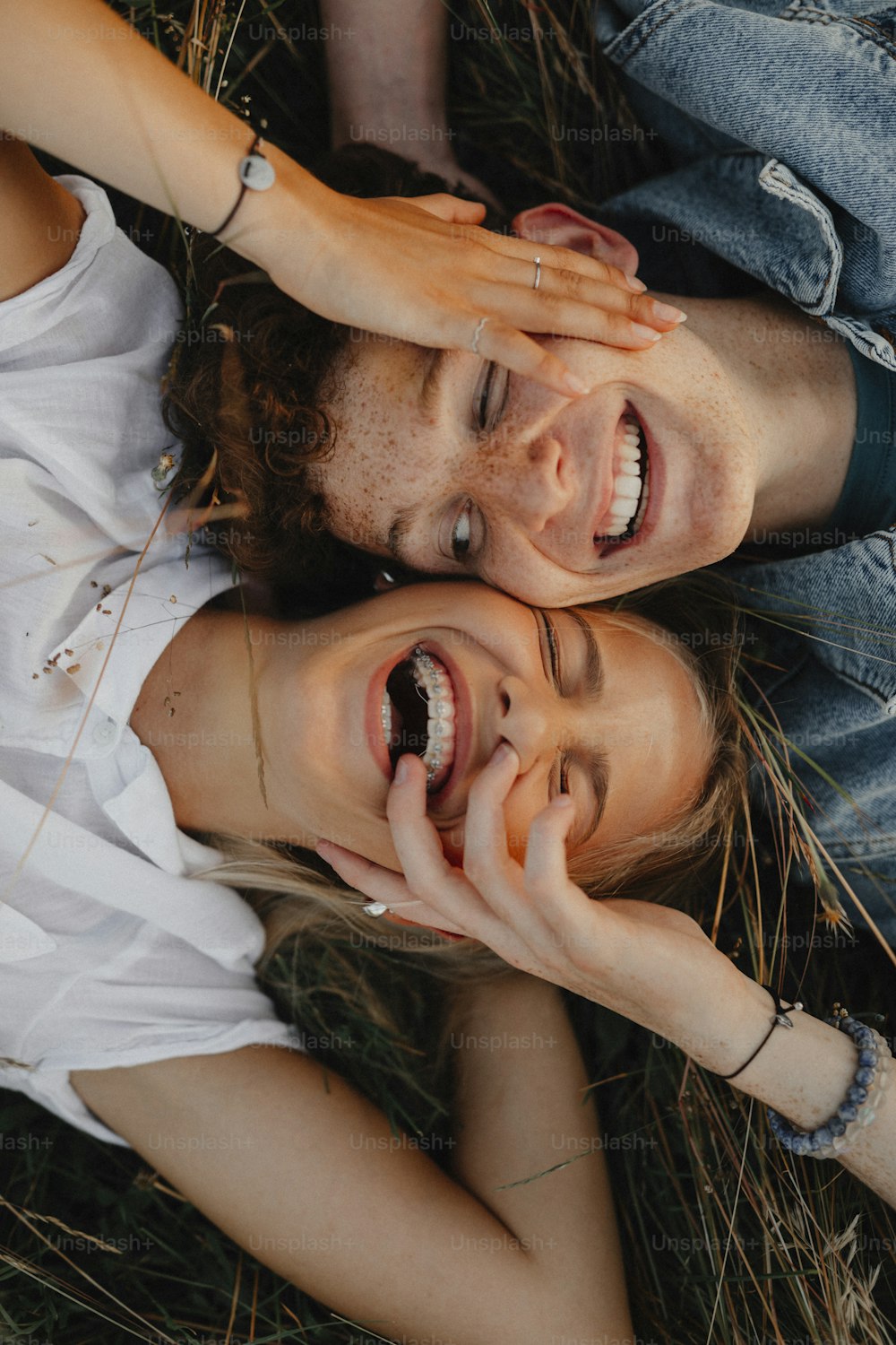 A top view of young couple on a walk in nature in countryside, lying in grass laughing.