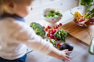 Niño pequeño en la cocina. Un niño pequeño sentado en una mesa con verduras.