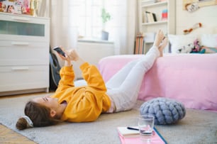 Happy young girl with smartphone on floor at home, making video call.