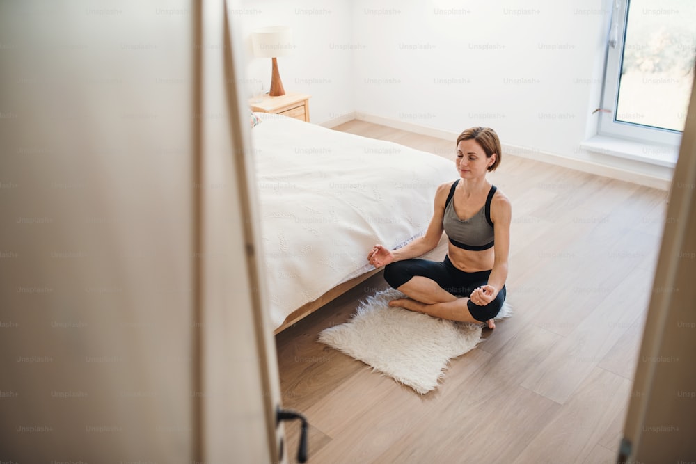 Eine hochschräge Ansicht einer jungen Frau, die drinnen in einem Schlafzimmer Yoga macht. Speicherplatz kopieren.