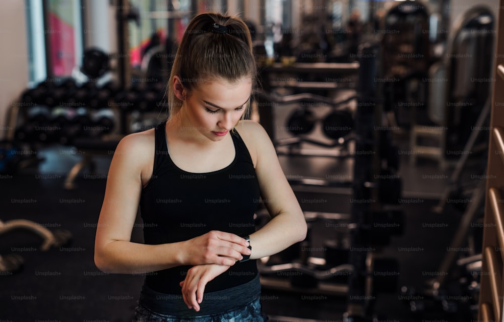 Young girl or woman doing workout in a gym, using a smartwatch.