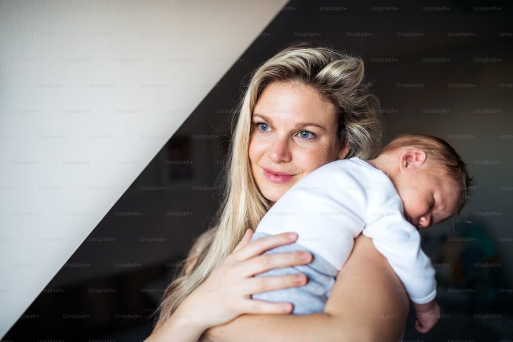 Una bella giovane madre che tiene in braccio un neonato addormentato a casa. Copia spazio.