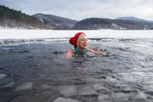 A front view of active senior woman swimming outdoors in water in winter, cold therapy concept.