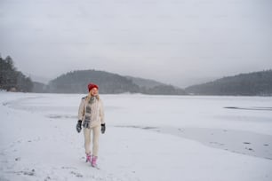 Una mujer mayor activa en caminata al aire libre en la naturaleza nevada, caminando por un lago congelado.