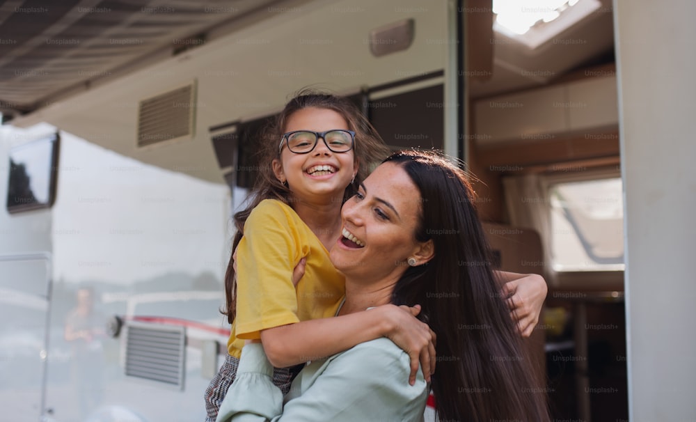 Una madre abrazando a su hija en coche al aire libre en el campamento al anochecer, viaje de vacaciones familiares en caravana.