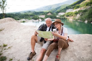 A happy senior couple on hiking trip on summer holiday, using map.