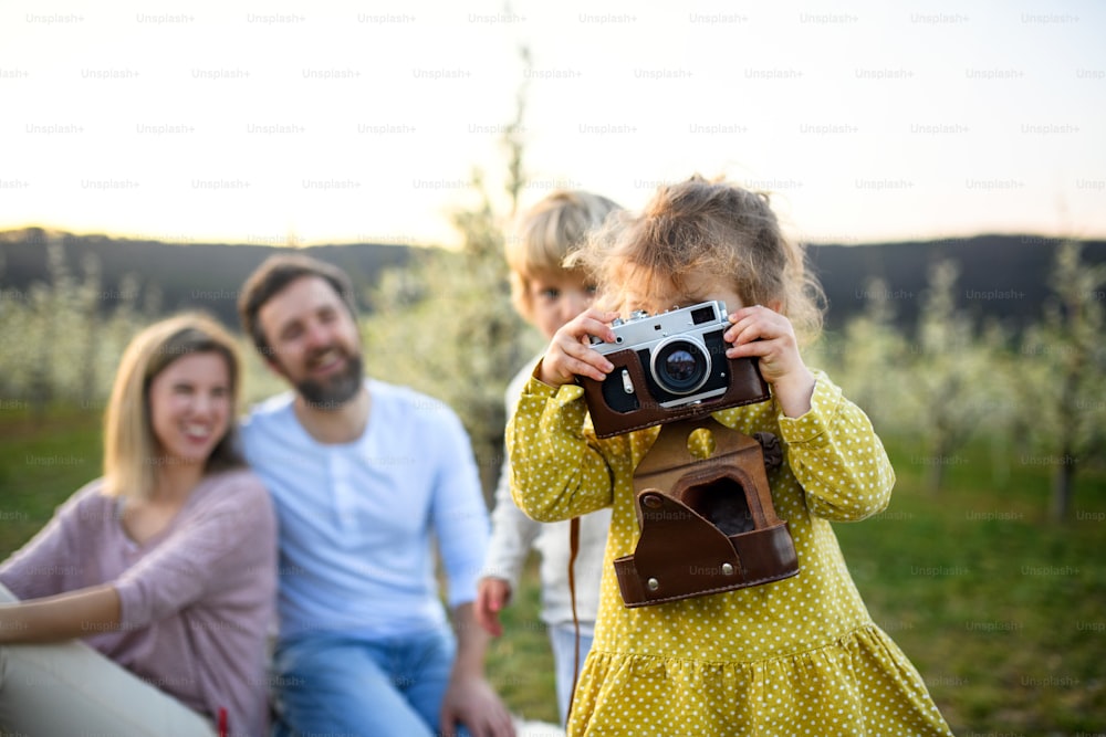 Familie mit zwei kleinen Kindern, die draußen in der Frühlingsnatur sitzen und Fotos machen.