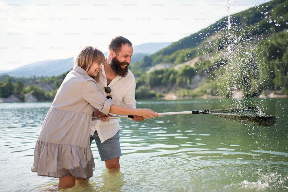 Happy preteen girl and mature father with fishing net on summer holiday by lake.