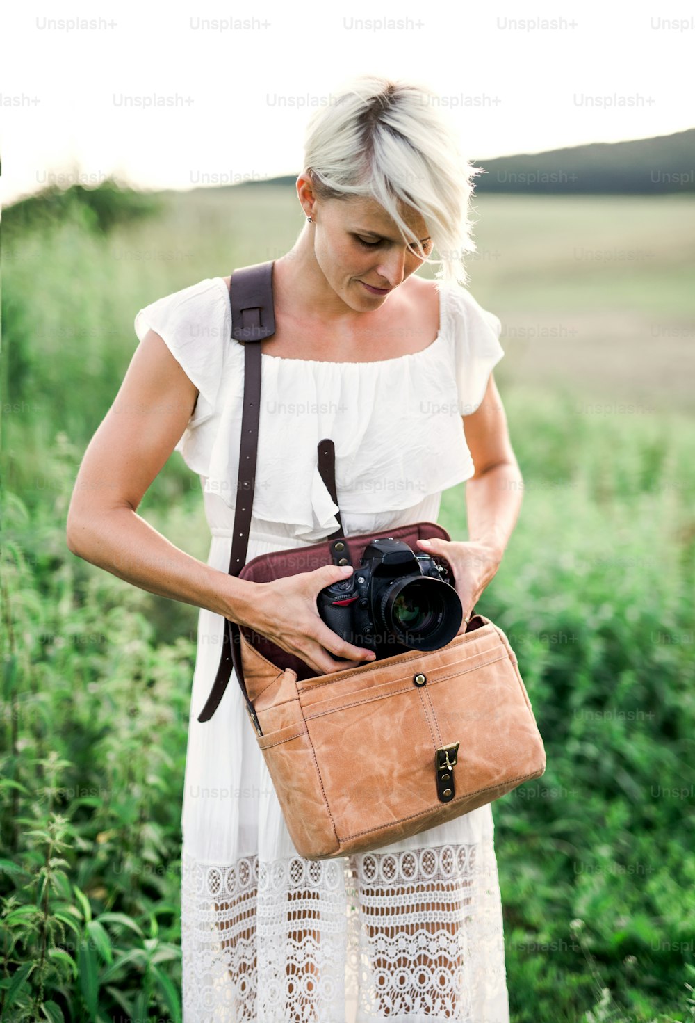 茶色の革のバッグからカメラを取り出す自然界の若い女性の正面図。