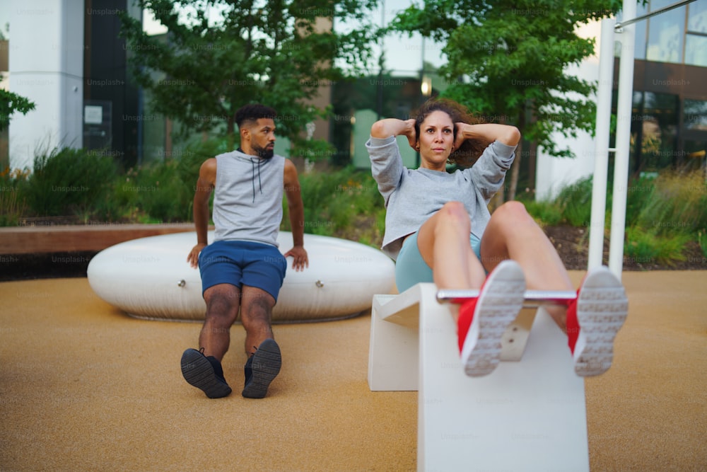 Um casal de amigos do homem e da mulher fazendo exercícios ao ar livre no parque de exercícios da cidade