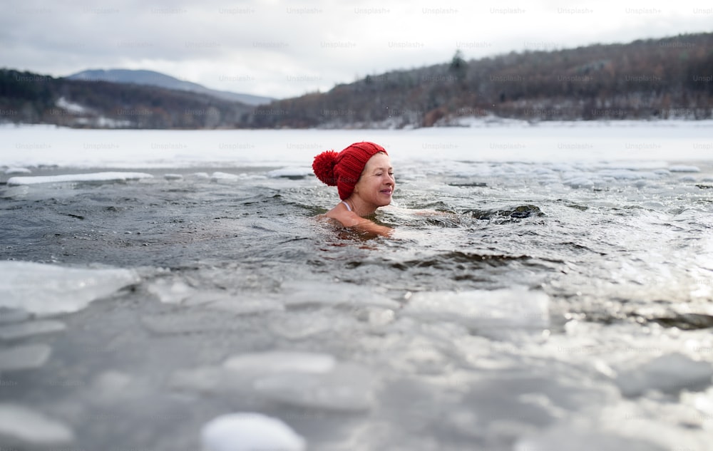 Uma mulher idosa ativa feliz no chapéu mergulhando ao ar livre na água no inverno, conceito de terapia fria. Espaço de cópia.