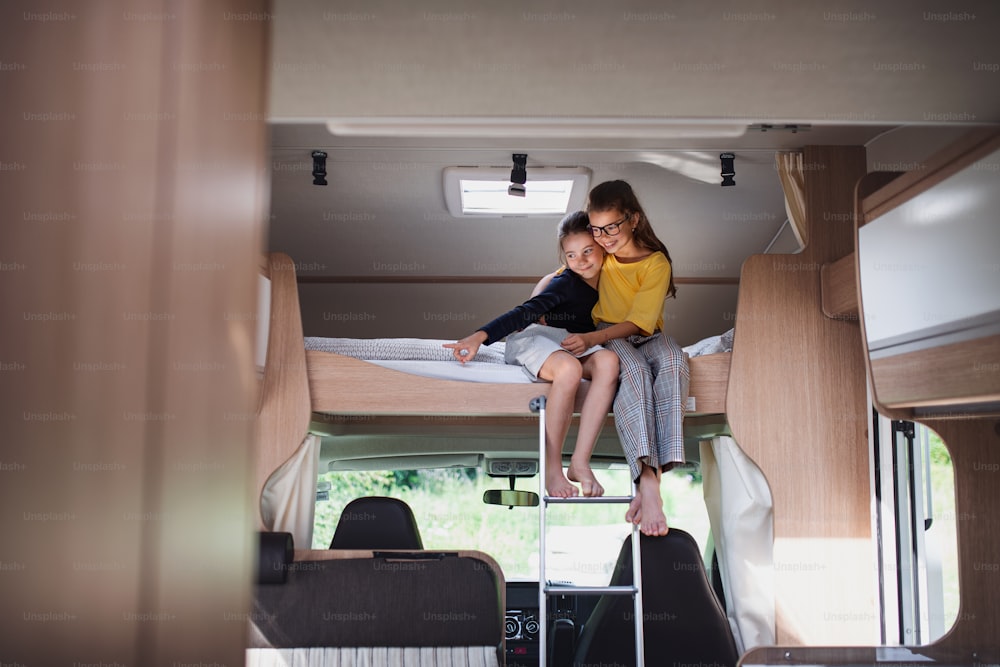 Hermanas felices de las niñas pequeñas sentadas en la cama en el interior de la caravana, viaje de vacaciones familiares.