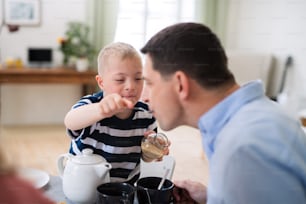 A down syndrome boy with father at the table, feeding father when having breakfast.