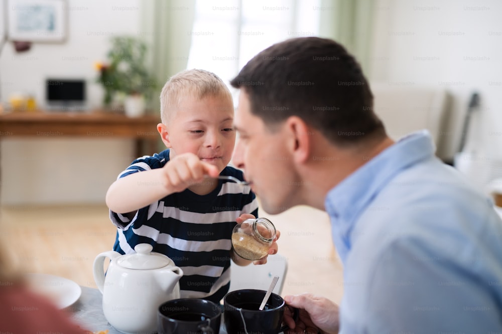A down syndrome boy with father at the table, feeding father when having breakfast.