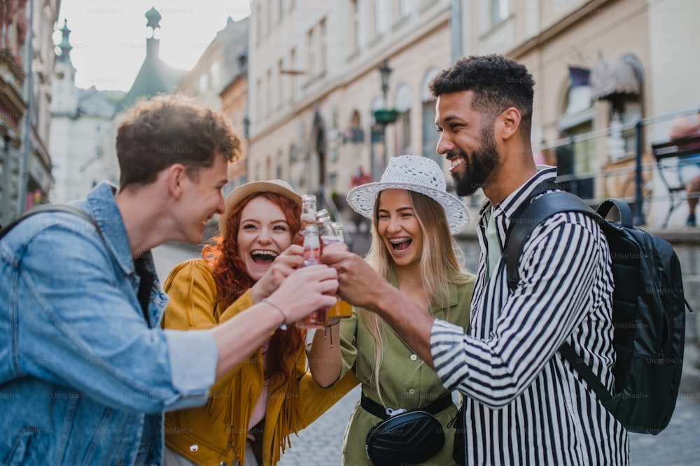 Una vista frontale di un gruppo di giovani felici con bevande all'aperto in strada durante la gita in città, ridendo.