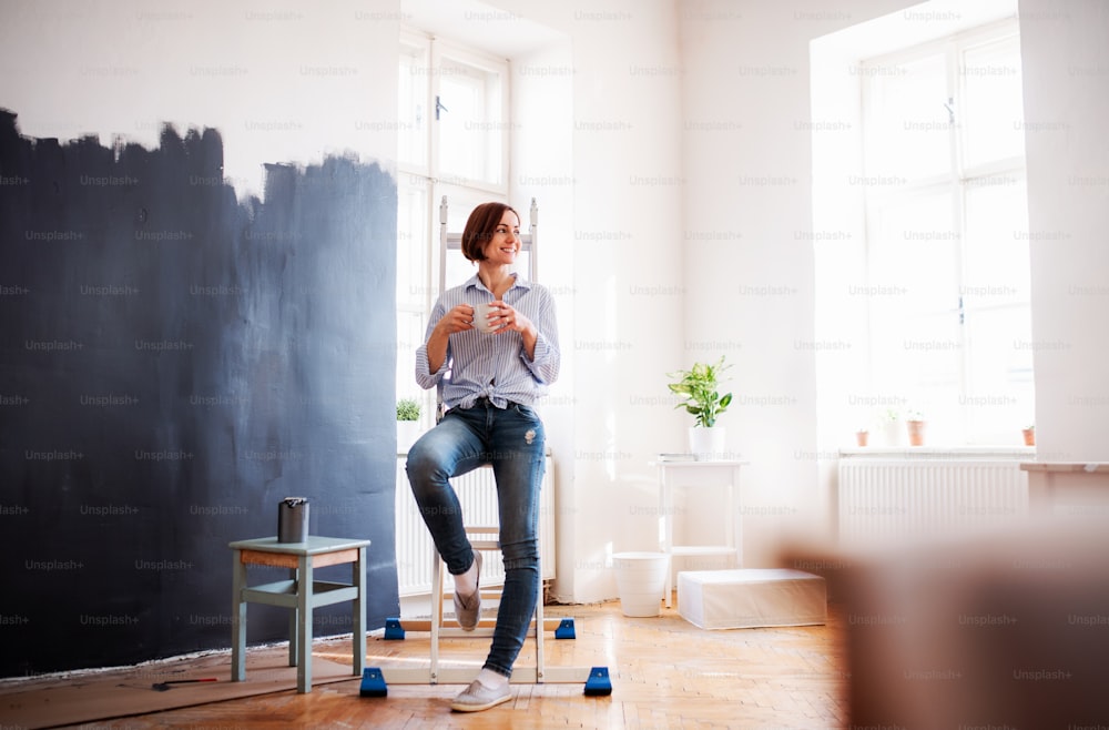 A portrait of young creative woman with a cup of coffee painting wall black. A startup of small business.