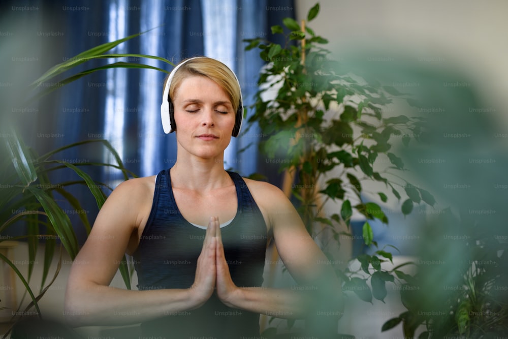 Front view of young woman with headphones indoors at home, doing yoga exercise. Copy space.