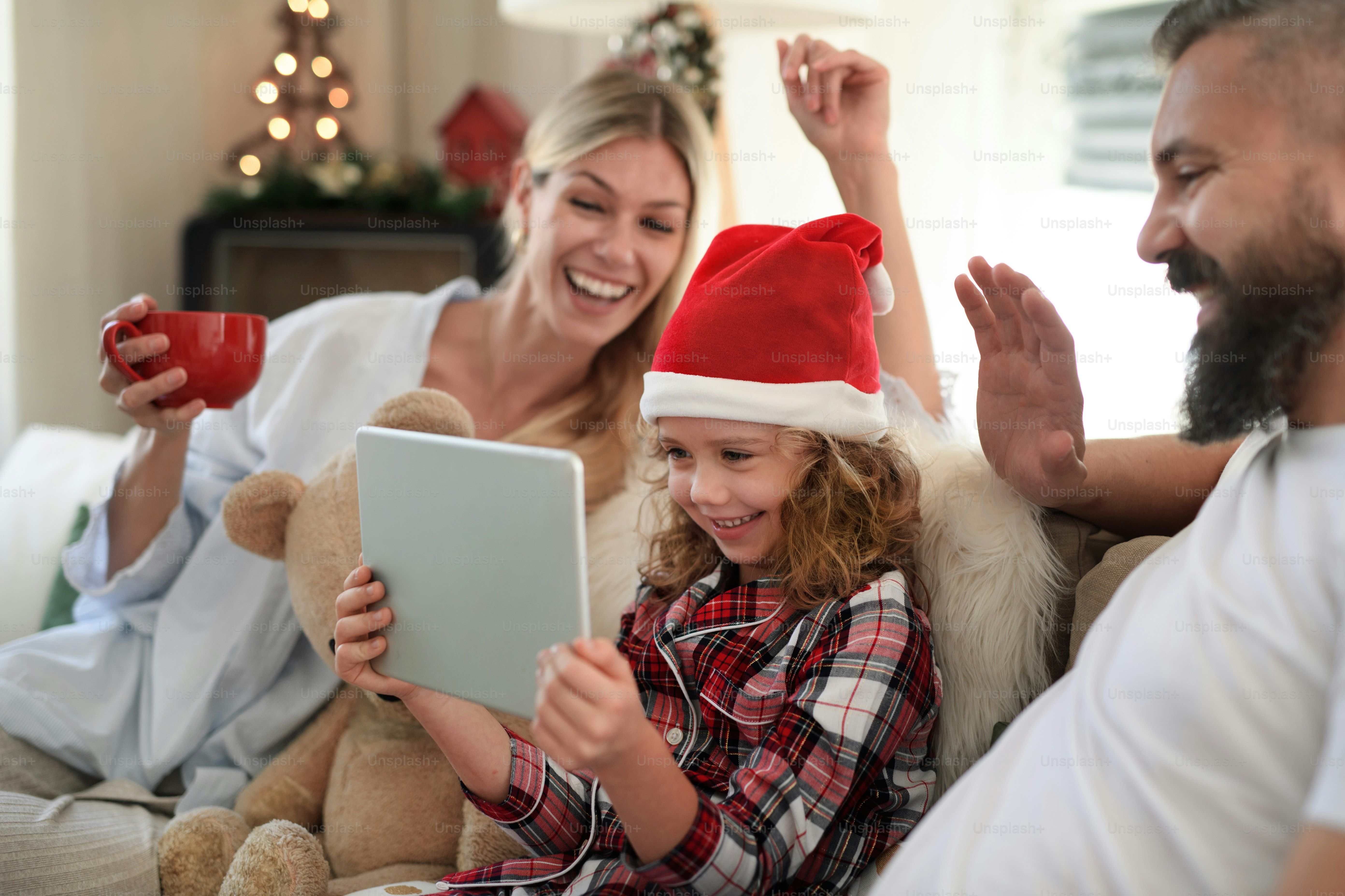 Family with small daughter indoors at home at Christmas, having video call on tablet.