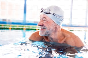 Senior man in an indoor swimming pool. Active pensioner enjoying sport.