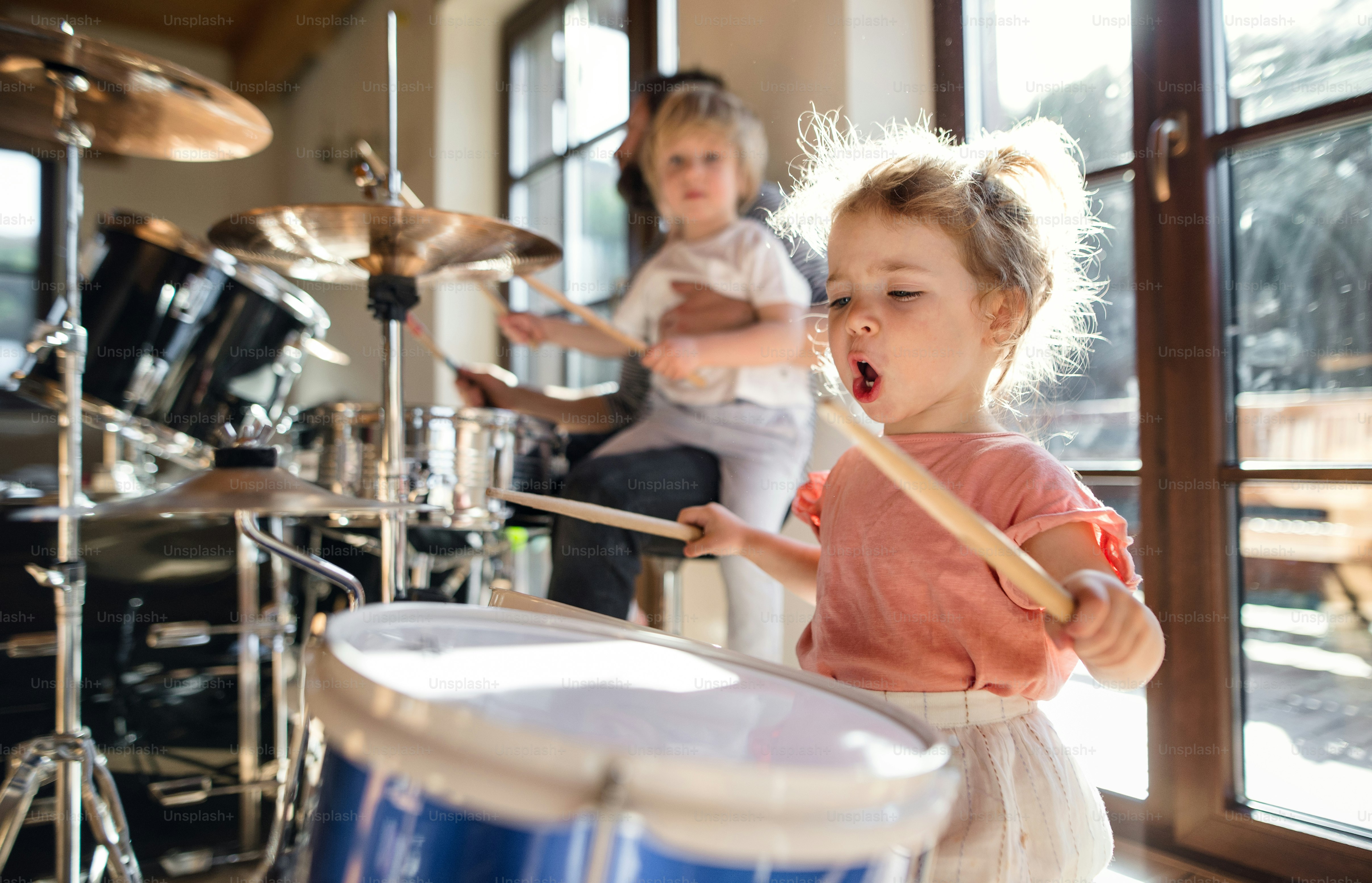 Portrait of happy small girl indoors at home, playing drums